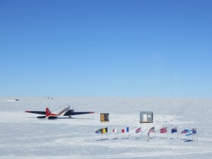 Ceremonial South Pole, surrounded by the flags of the Antarctic Treaty nations, with a tourist plane in the background.